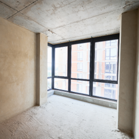 before Unfinished apartment interior with raw concrete walls and large windows.